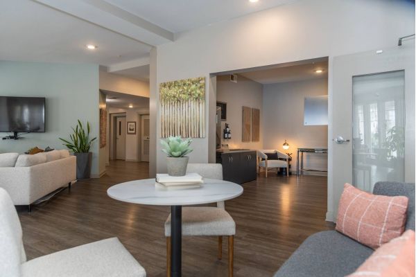 Modern living space with neutral decor, a round table, sofa, plants, and wall art on light-colored walls.