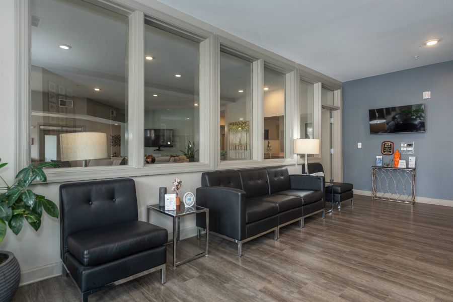 Modern waiting room with black leather chairs, a sofa, lamps, plants, and wood flooring.