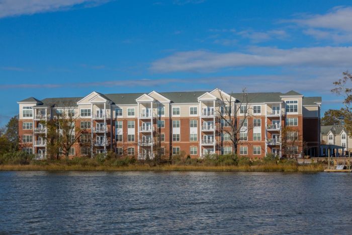 Attain on 5th apartment homes with Four-story apartment building with balconies, facing a body of water under a blue sky.