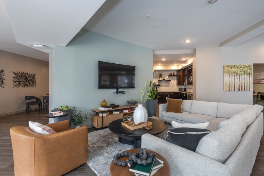 Modern room with a sectional sofa, armchair, TV on wall, and open kitchen in the background.