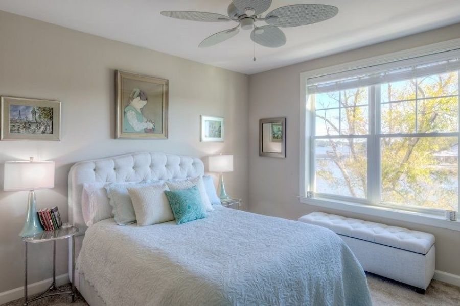 Bright bedroom with a white bed, art on pale walls, and a large window letting in natural light.