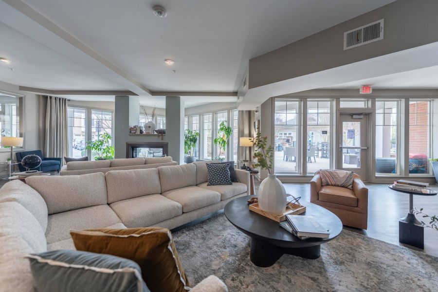 Modern living room with a large beige sectional sofa, armchair, coffee table, and large windows letting in light.