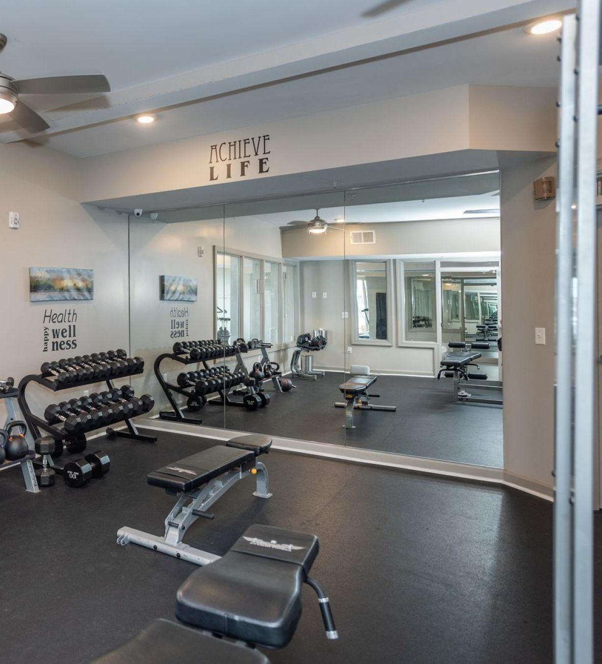 Attain on 5th apartment homes with Small gym room with dumbbells, benches, kettlebells, mirrors, and cardio equipment near windows.