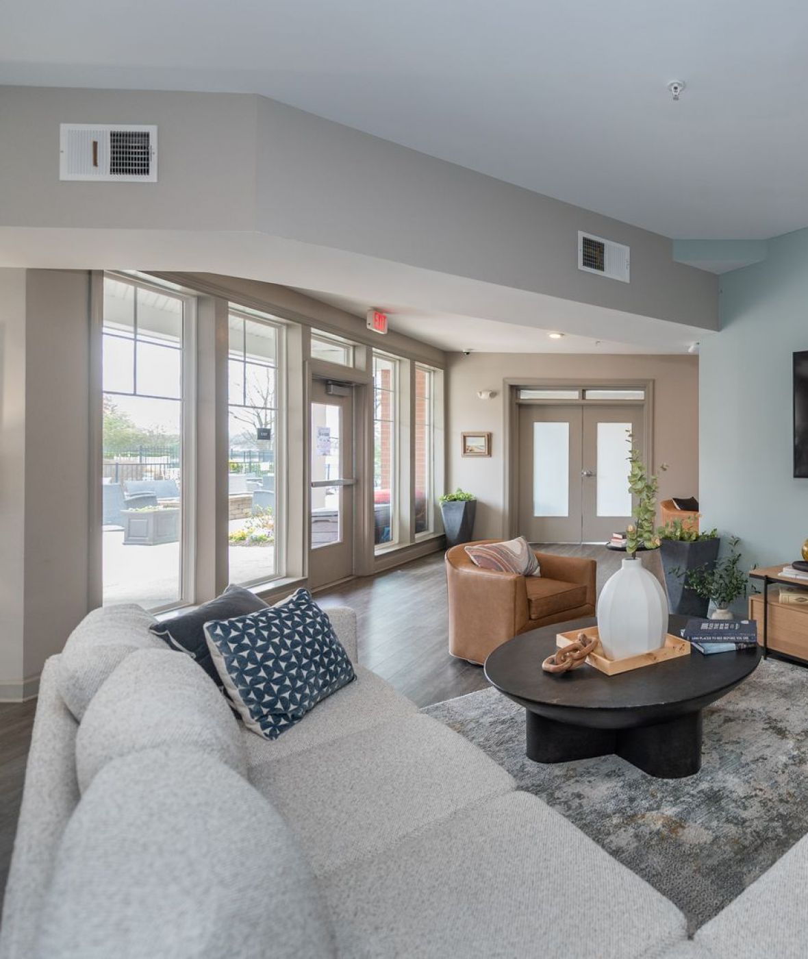 Attain on 5th apartment homes with Modern living room with a sectional sofa, coffee table, wall-mounted TV, plants, and large windows.