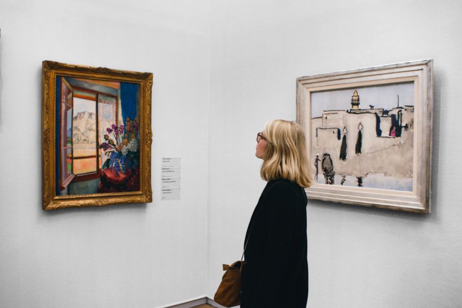 A woman observes colorful paintings hanging on the white walls of an art gallery.
