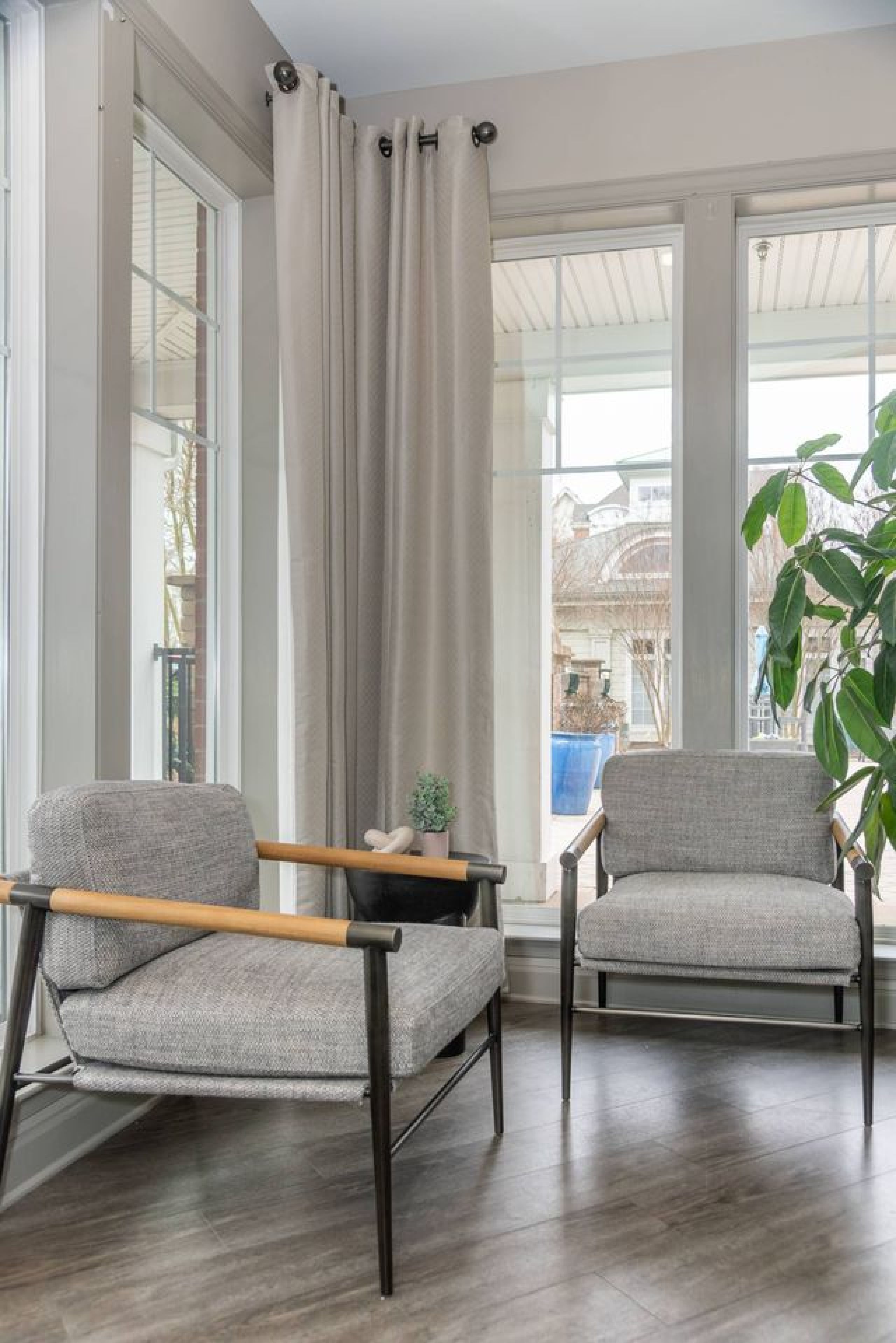 Two modern gray armchairs near tall windows with beige curtains and a plant in a bright room.